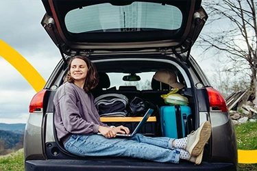 Person Sitting with Laptop In Open Boot Of Car